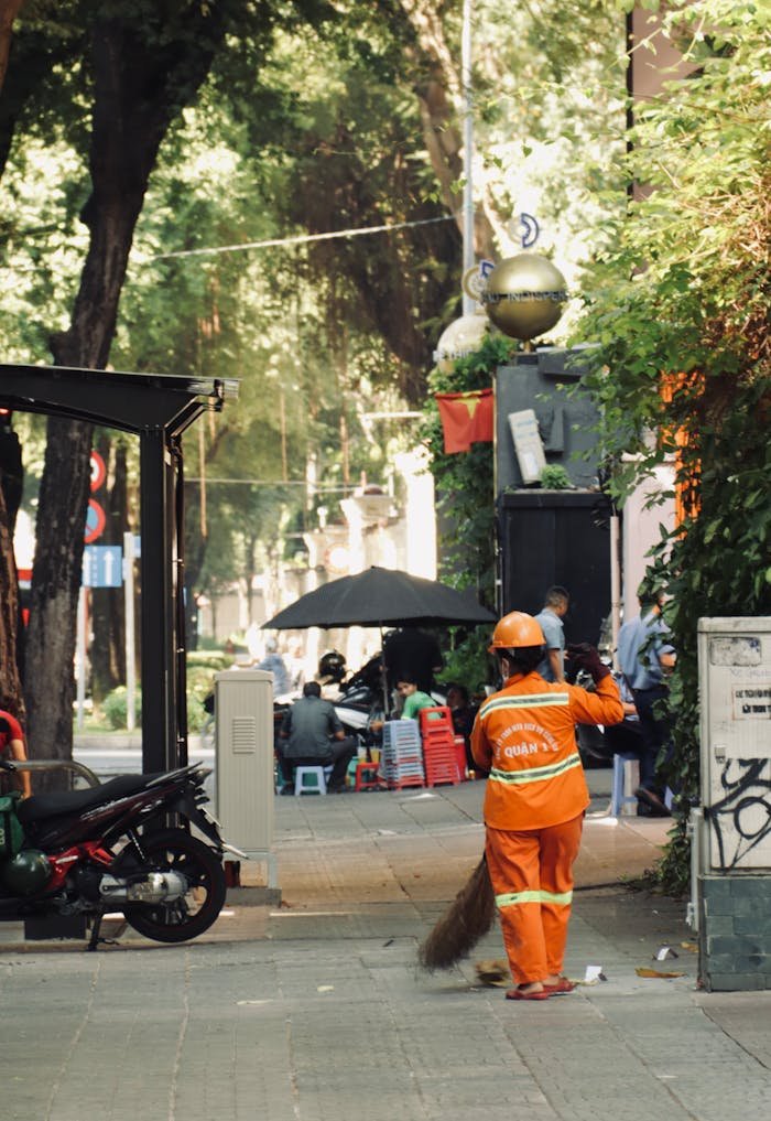 zipwp-image-20381388 A man in orange clothing is sweeping the sidewalk